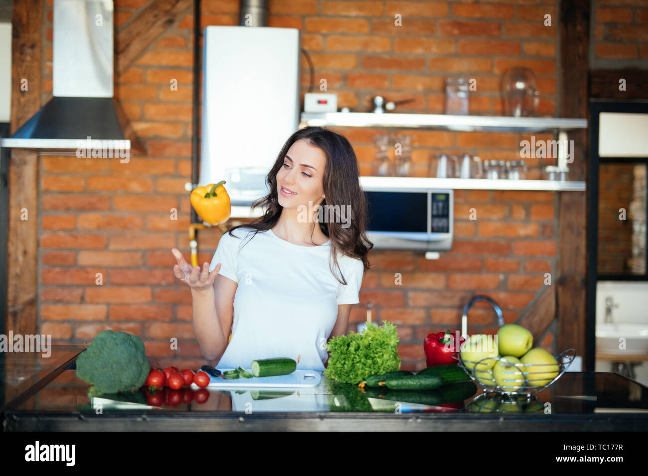 During active conversation. Chatty lady playing with vegetables while talking on mobile phone on her modern kitchen Stock Photo