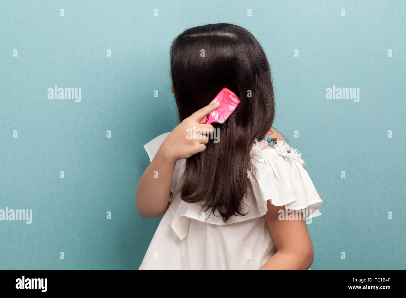 Side view portrait of teenager girl in white dress standing, making attention and combing brunette hair with pink hairbrush. Morning care. Indoor, iso Stock Photo