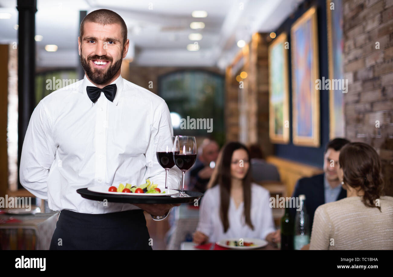 Professional friendly smiling pleasant waiter holding serving tray for ...
