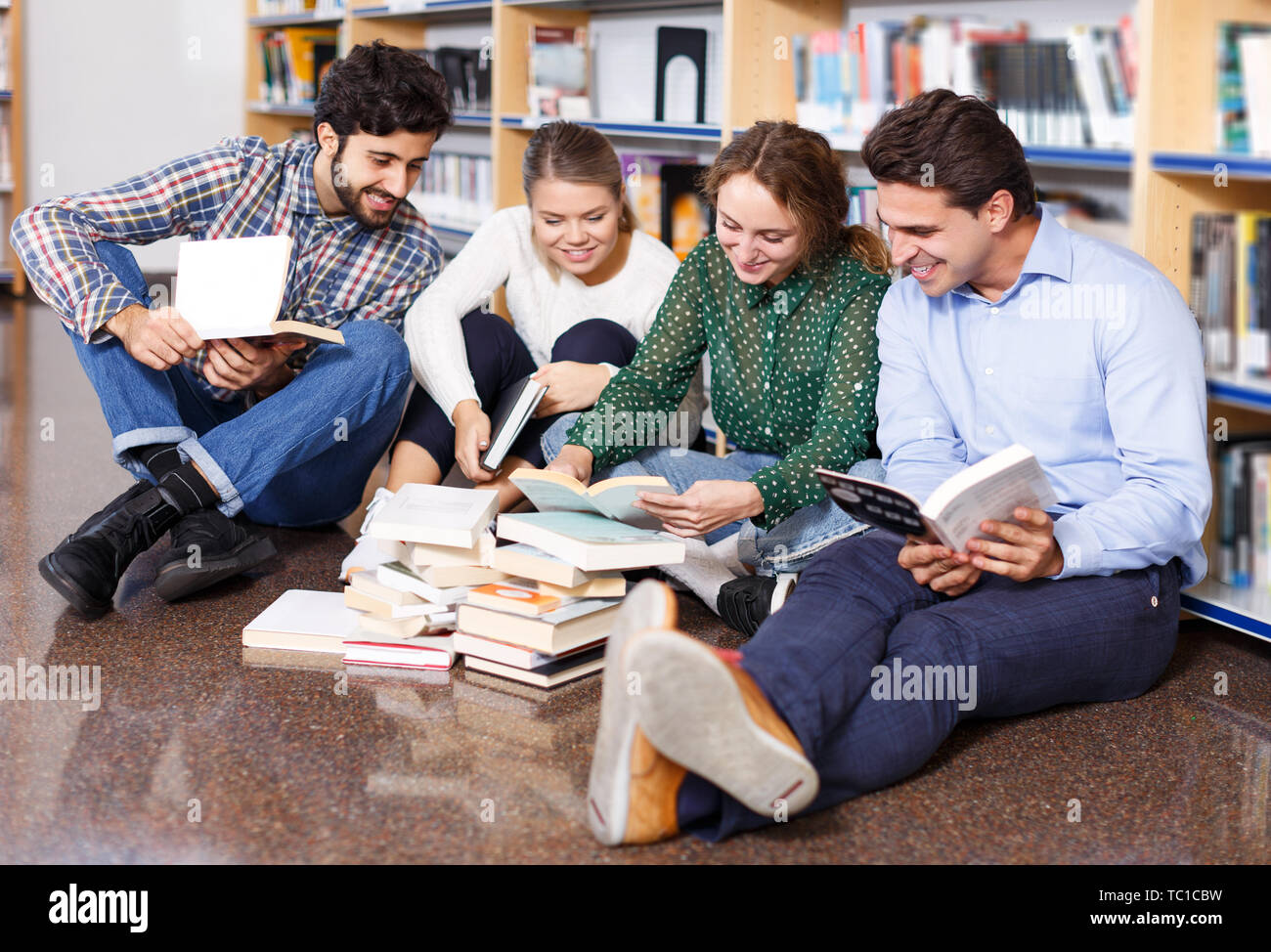 Four Happy Students Sitting On Floor In Library In Campus And