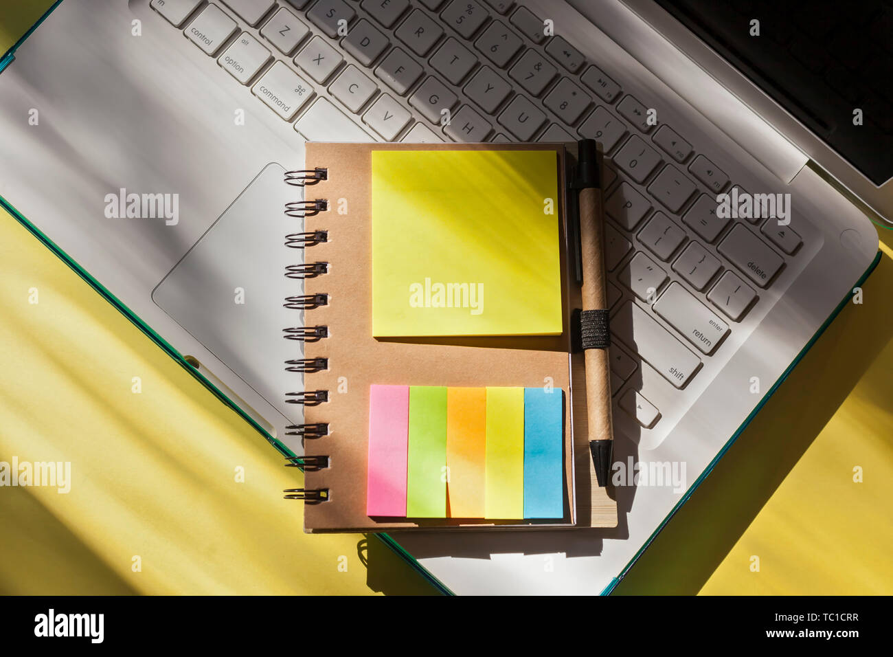 Top view of Spiral Notebook with Pen in Holder with colorful sticky page markers- Workspace with laptop Stock Photo