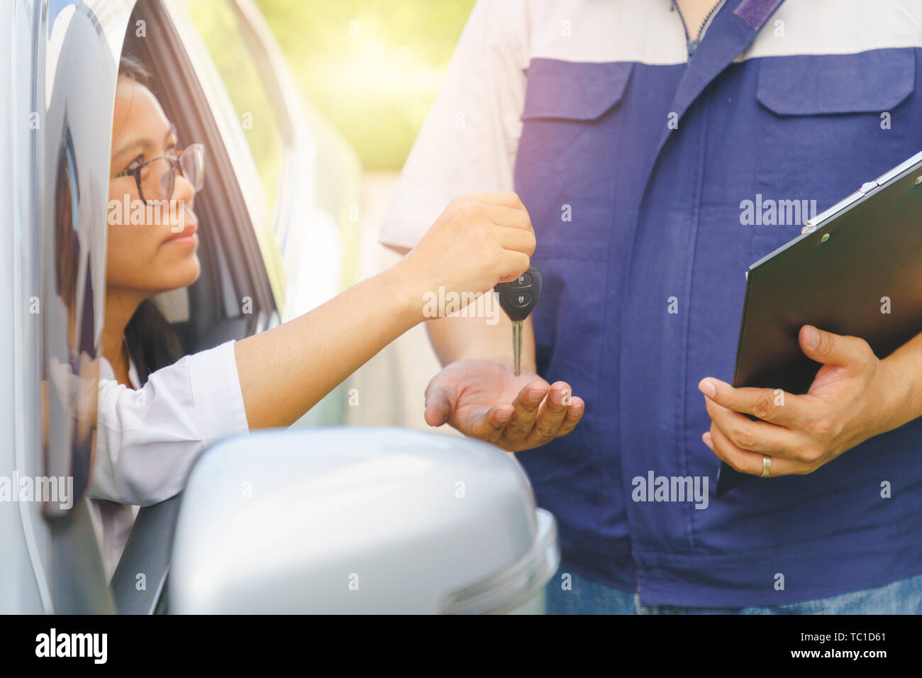 Asian Woman sitting in the broken car the keys giving to the car mechanic for maintenance in the garage. Sunlight and flare background concept. Stock Photo
