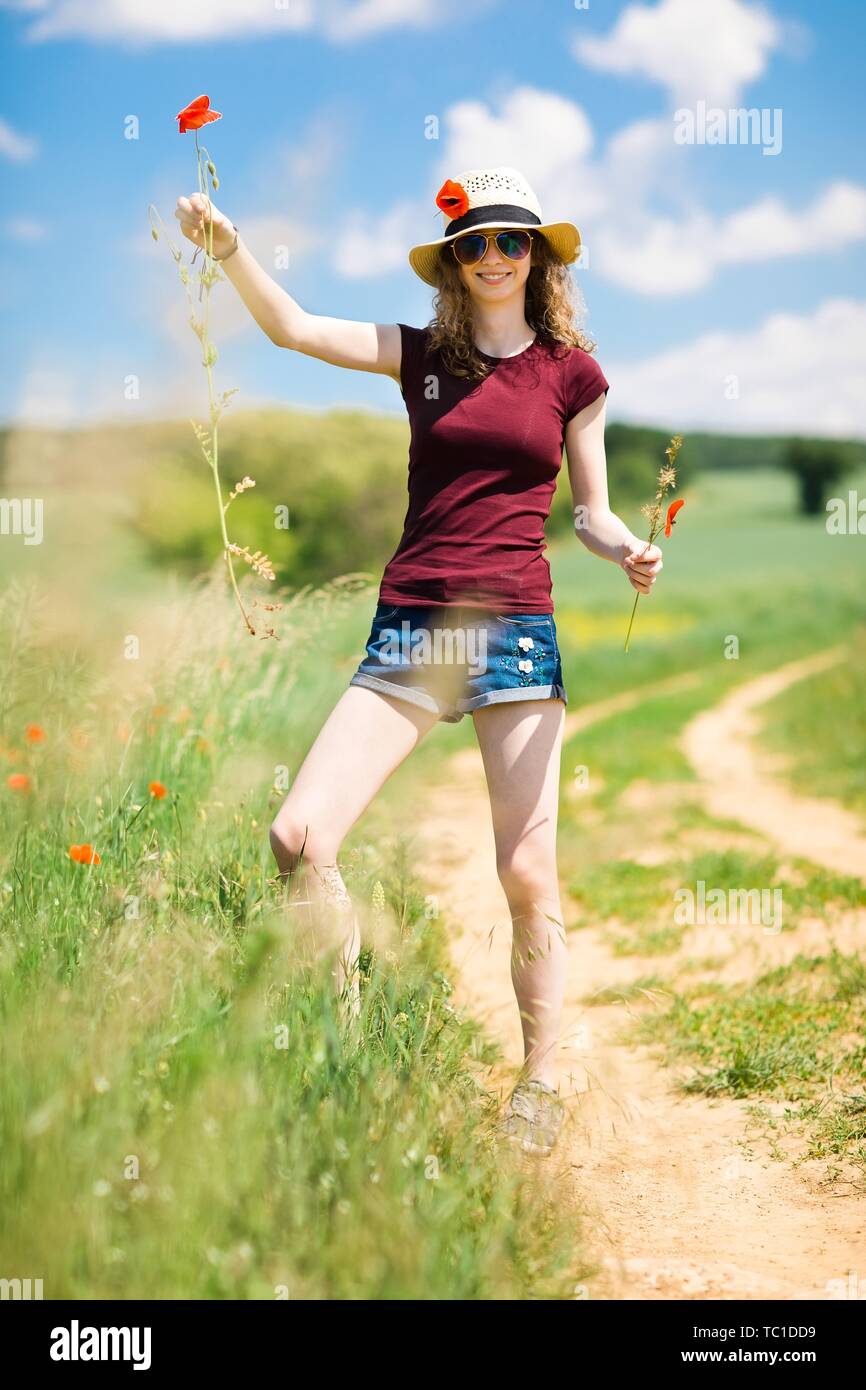 A young girl in hat rip out poppy flower with roots, sunny day Stock Photo