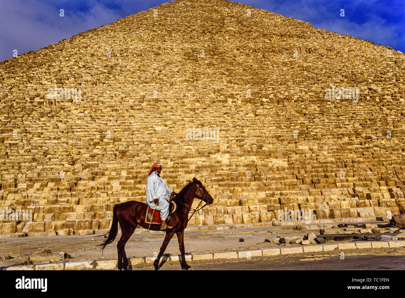 Photo: © Simon Grosset. The Giza Pyramid complex, or Giza Necropolis, near Cairo, Egypt.  A man rides a horse in front of the Great Pyramid of Giza, o Stock Photo