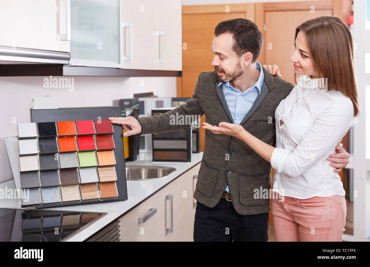 Young Family Couple Choosing Material For Kitchen Furniture In