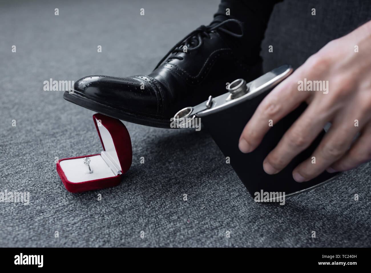 cropped view of man holding flask and trampling gift box with ring Stock Photo