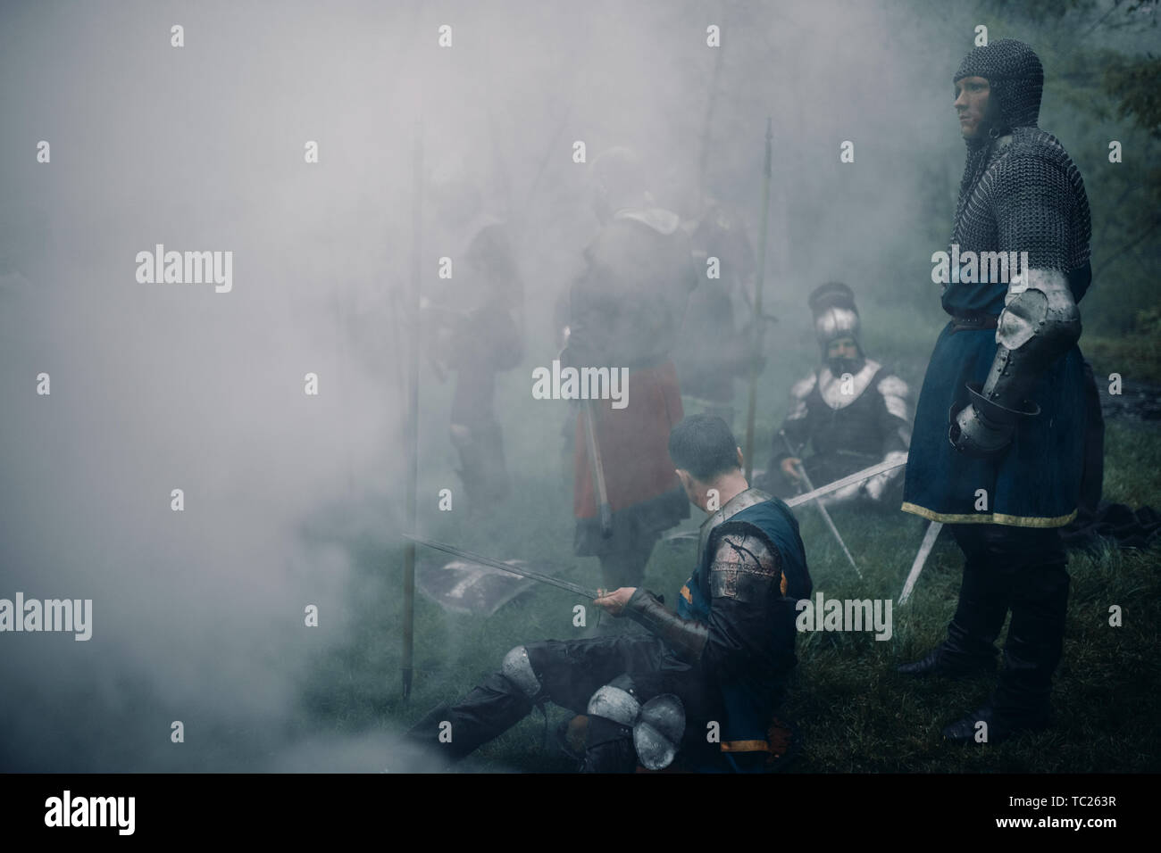 Battle squad of medieval knights of the Crusaders rest on the halt against background of of a misty forest. Stock Photo