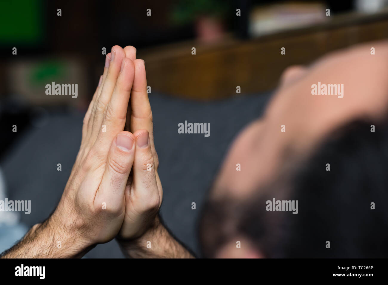 partial view of lonely man holding praying hands while sitting at home Stock Photo