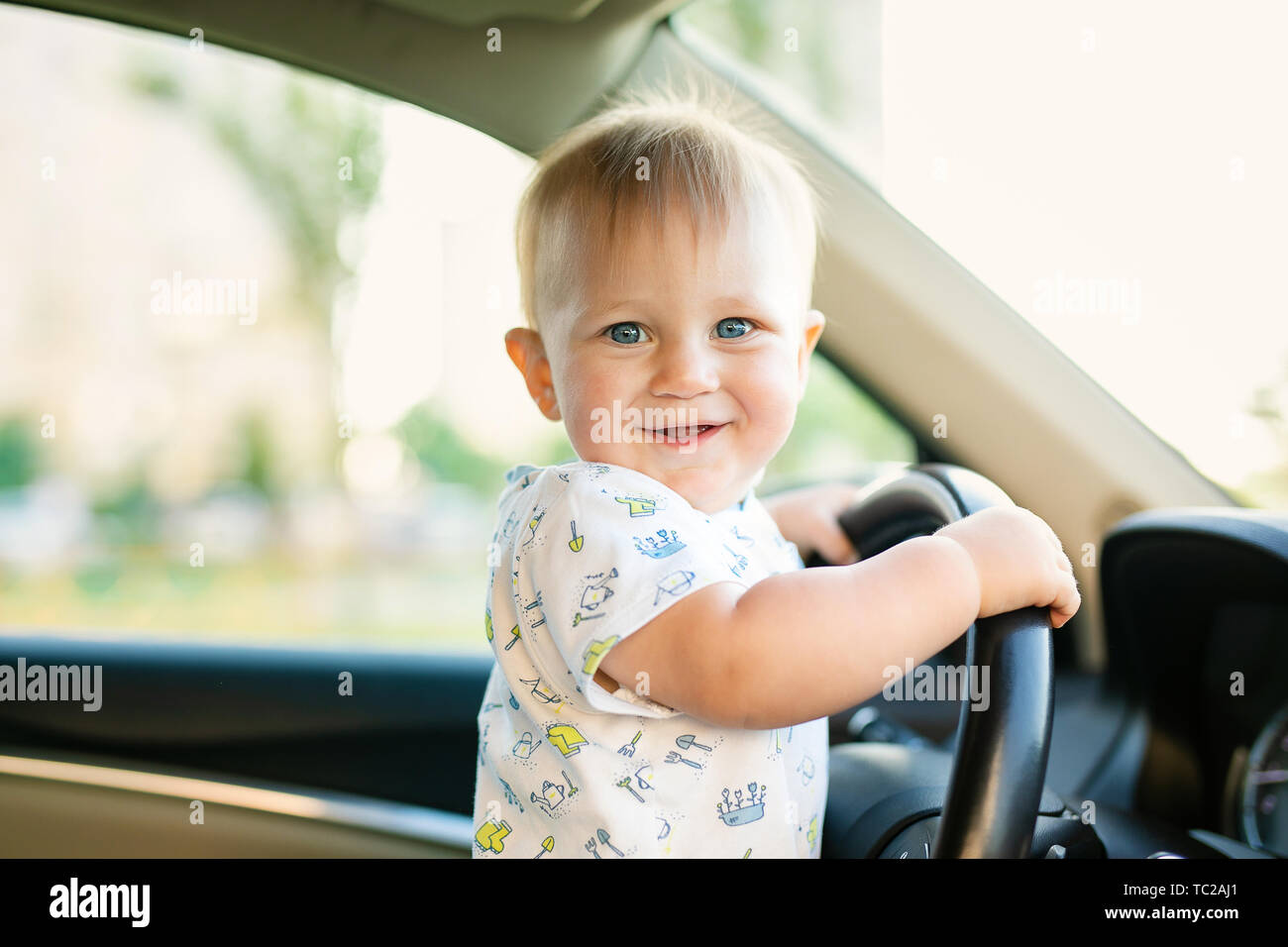 Cute little baby boy driving big car, holding steering wheel,smiling