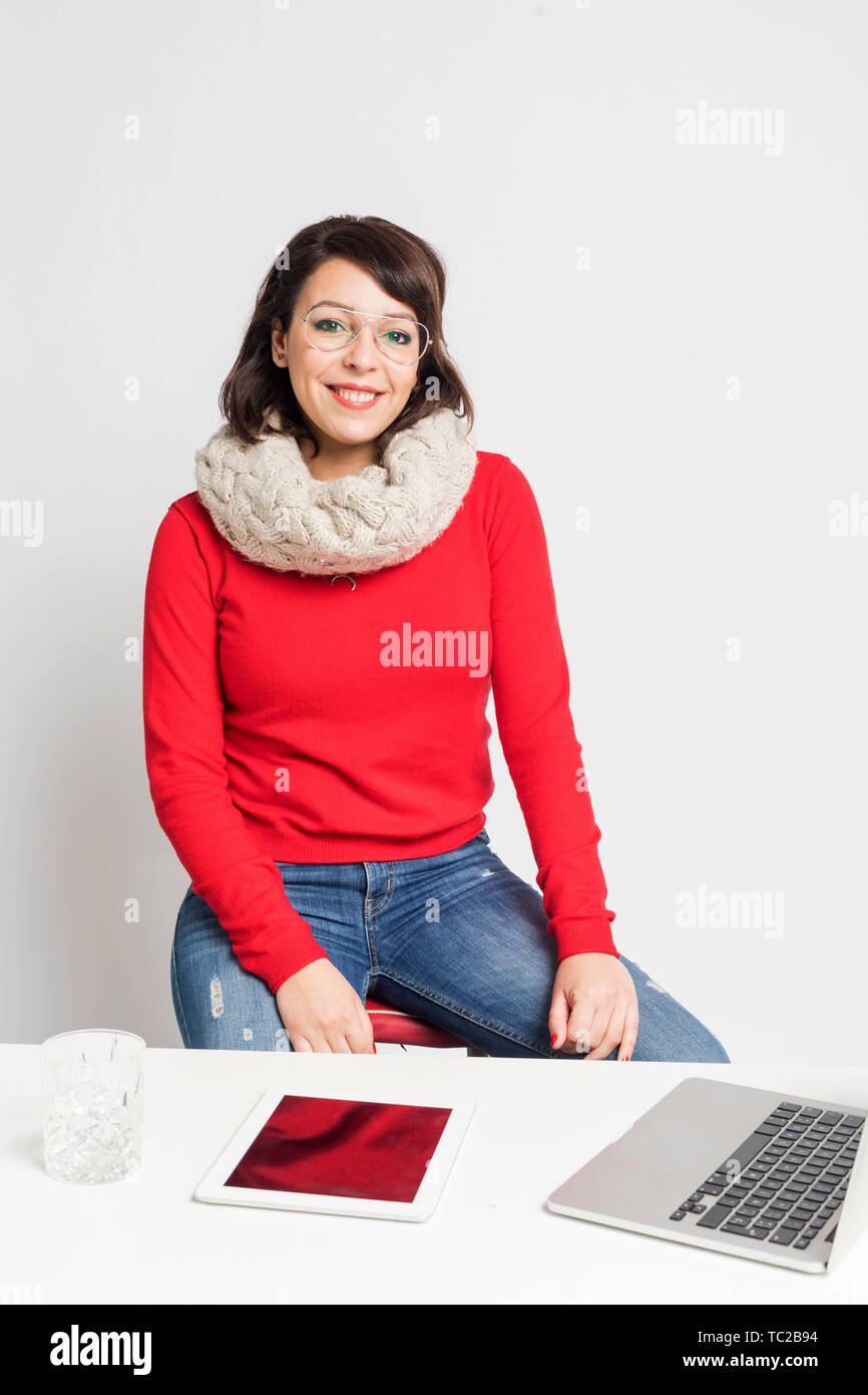 Front view of beautiful woman in casual wear sitting on a stool while looking camera against white background Stock Photo
