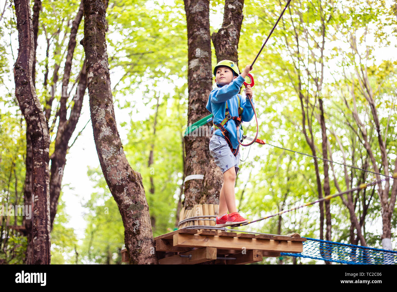 young boy passing cable route among trees, extreme sport in adventure park Stock Photo