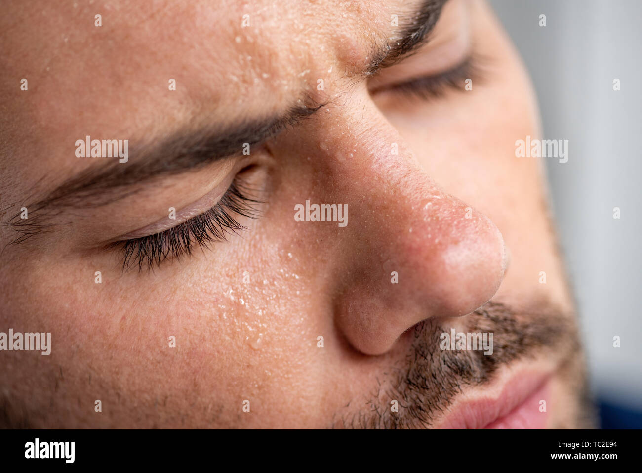 close up of man with sweaty face suffering from heat with closed eyes on grey Stock Photo