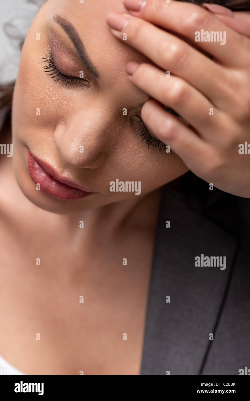 attractive woman suffering from heat and holding head on forehead with closed eyes on grey Stock Photo