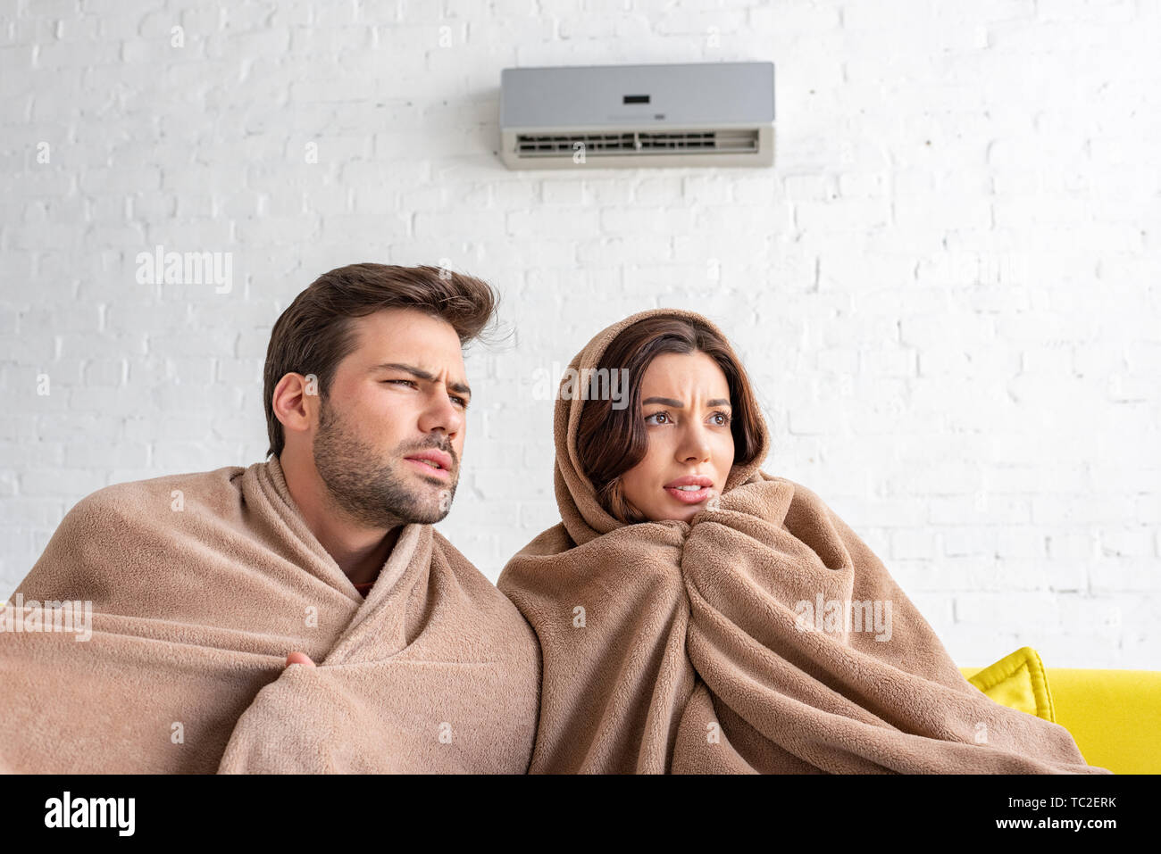 frozen man and woman warming under blankets while sitting under air  conditioner Stock Photo - Alamy
