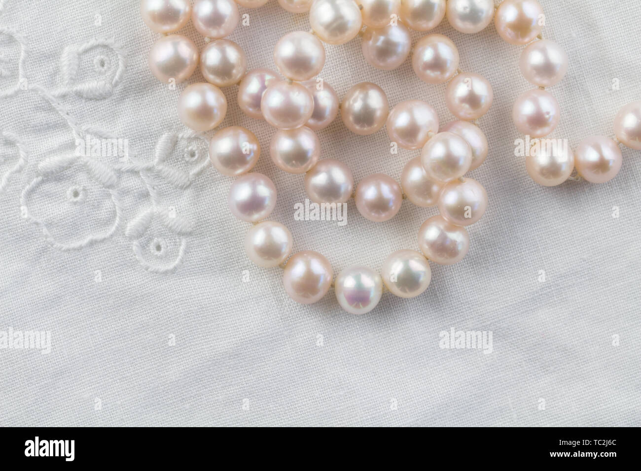 Pearl necklace on white embroidered linen background - top view photo of real pink pearls Stock Photo