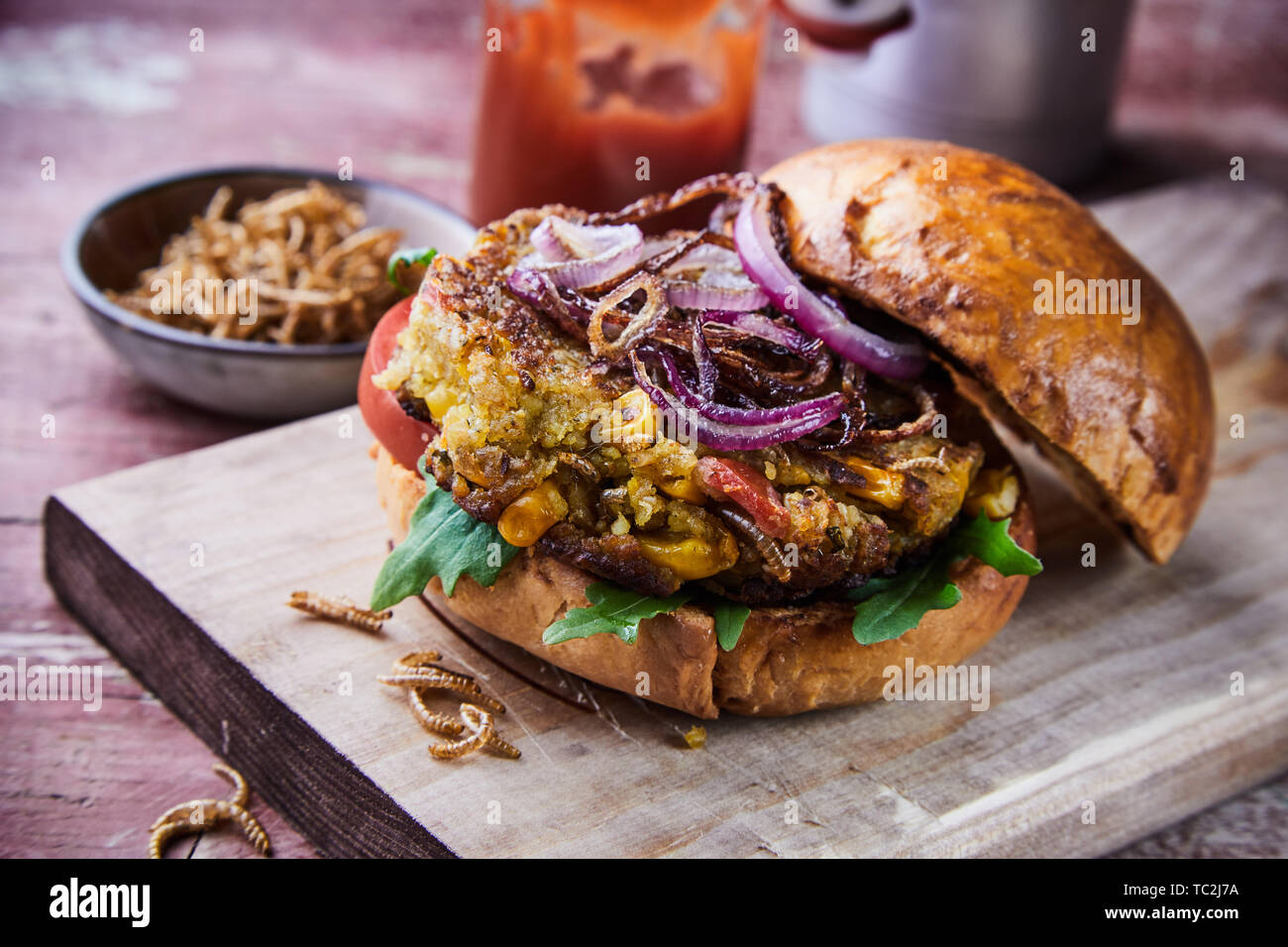 Speciality insect burger with fried mealworms and salad trimmings with rocket on a crusty fresh bun served on a wooden board suitable for a menu Stock Photo