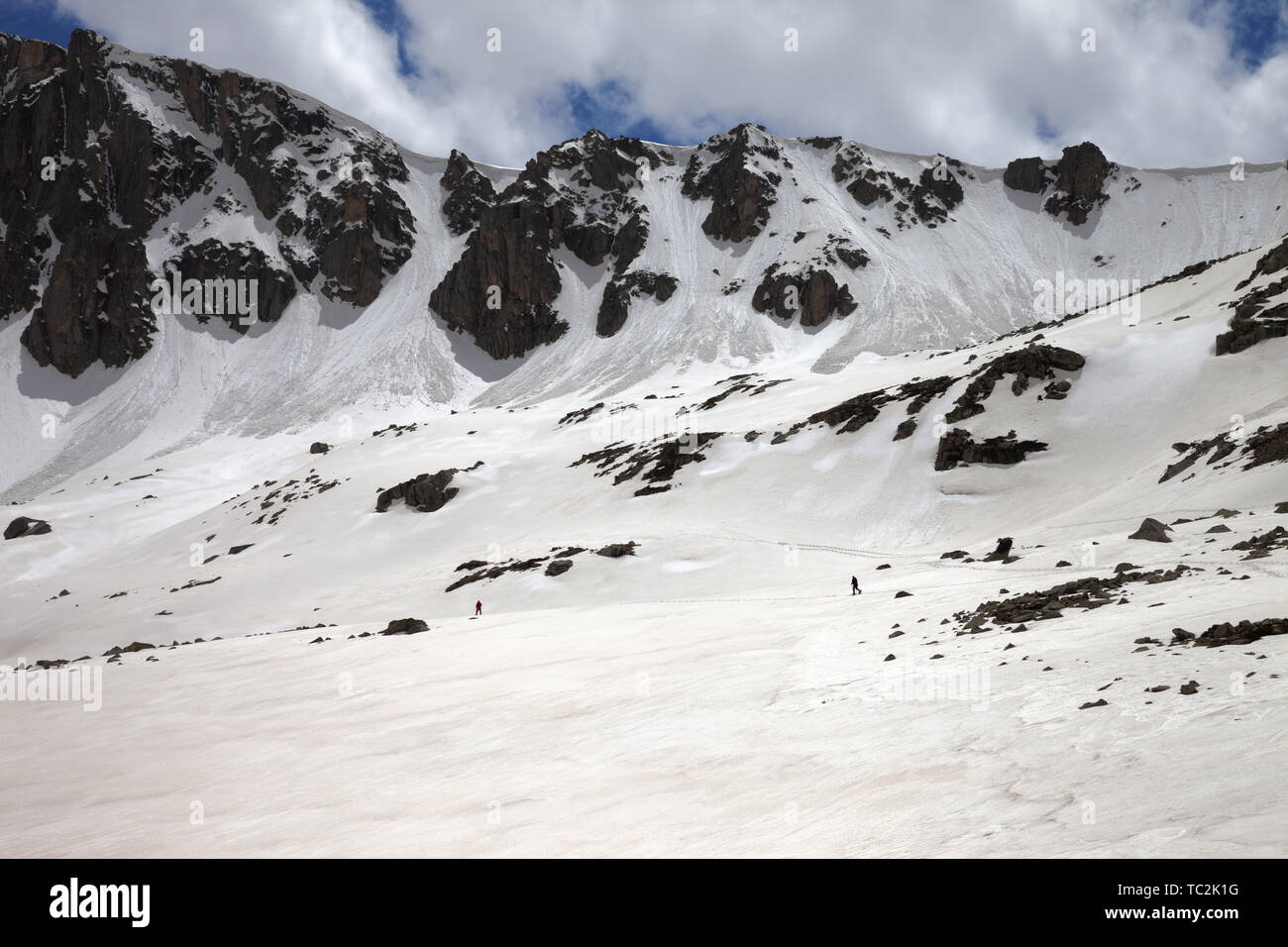 High mountains with snow cornice and avalanche trail, snowy plateau and two small silhouette of hikers at sunny day. Turkey, Kachkar Mountains, highes Stock Photo