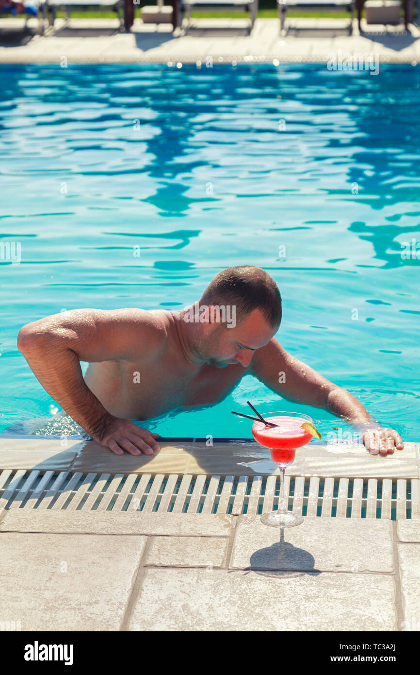 Man is swimming in swimming pool on holiday in Italy. Man is getting out of the swimming pool to drink alcohol pineapple cocktail Stock Photo