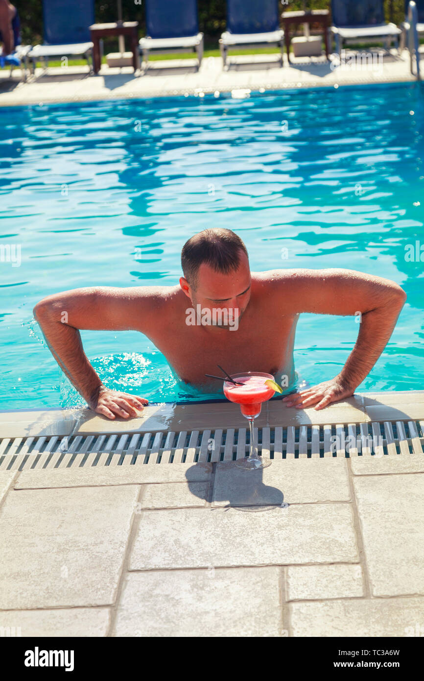 Man relaxing at swimming pool. A Front View of young boy enjoying the holiday in Greece at Swimming Pool and drinking fruit alcohol cocktail Stock Photo