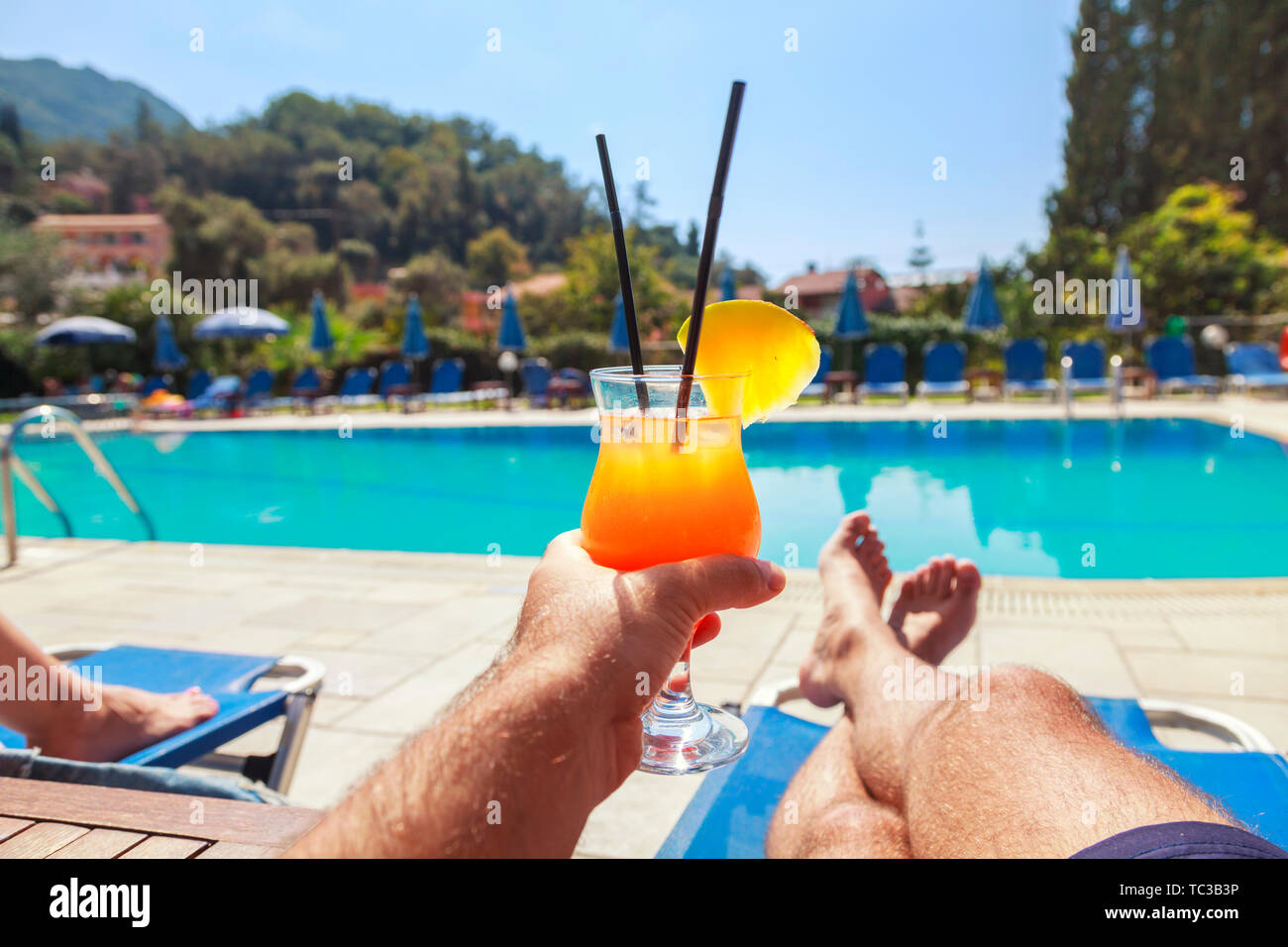 Young Man enjoying whit pineapple cocktail at the swimming pool. Man holding alcohol drink and lying on sunbed. Relax on Holidays Stock Photo