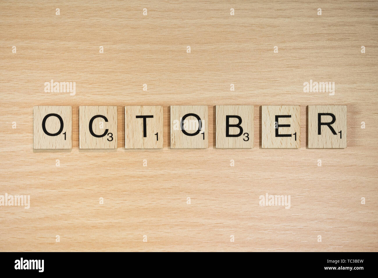 The word October, spelt out using wooden tiles on a wood effect background with scrabble numbered score values. Stock Photo