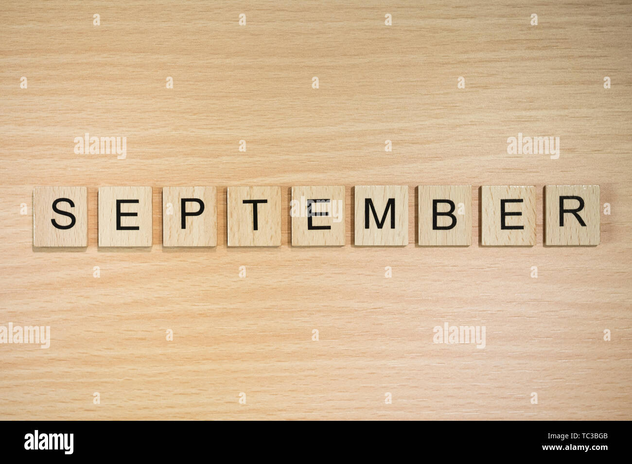The word September, spelt out using wooden tiles on a wood effect background. Stock Photo