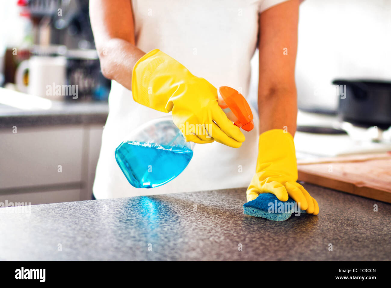 Woman Using Spray Polish To Clean Kitchen Surface. Woman cleaning kitchen Stock Photo
