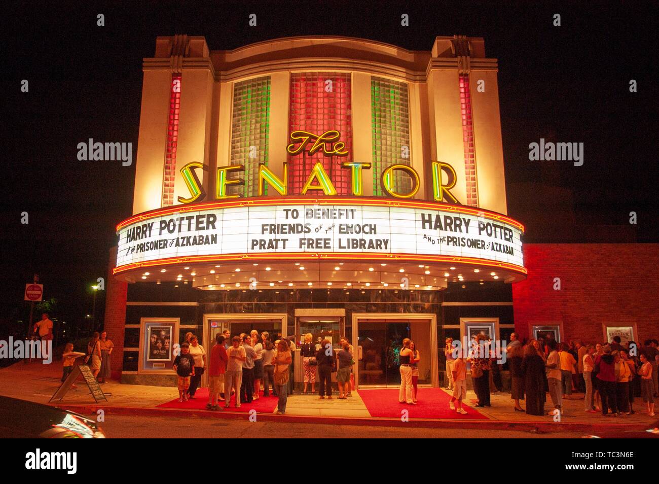 Night shot of a small crowd of movie patrons, standing outside the entrance and lit facade of the Senator Theatre, Baltimore, Maryland, June 3, 2004. From the Homewood Photography Collection. () Stock Photo