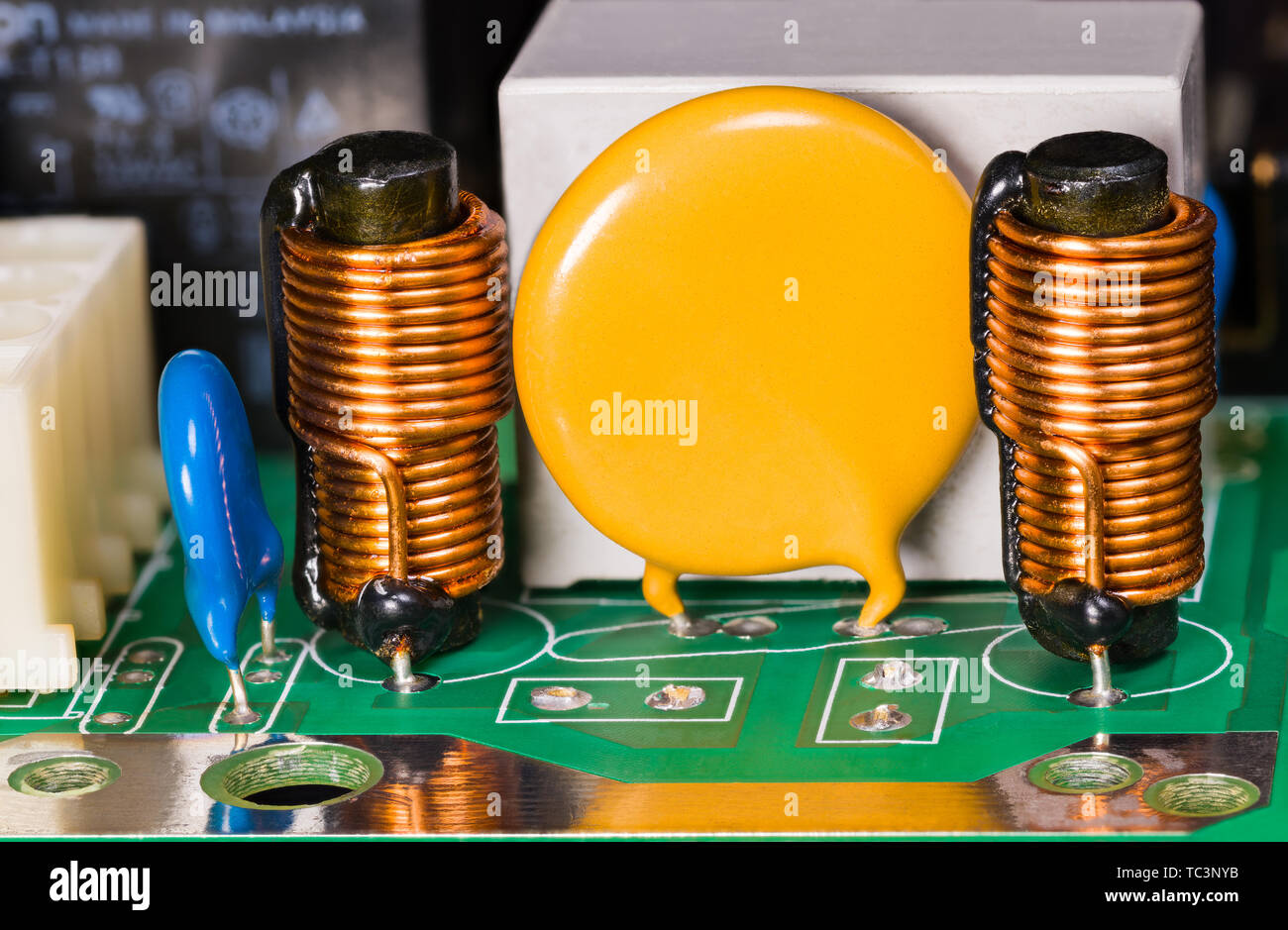 Varistor, cylindrical induction coils, capacitor and relay on green circuit board. Electro background with copy space on yellow round electronic part. Stock Photo