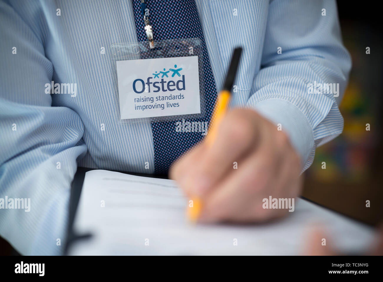 A man dressed in a shirt and tie with an Ofsted lanyard appears to be compiling a report using a pen and clipboard. (Editorial use only) Stock Photo