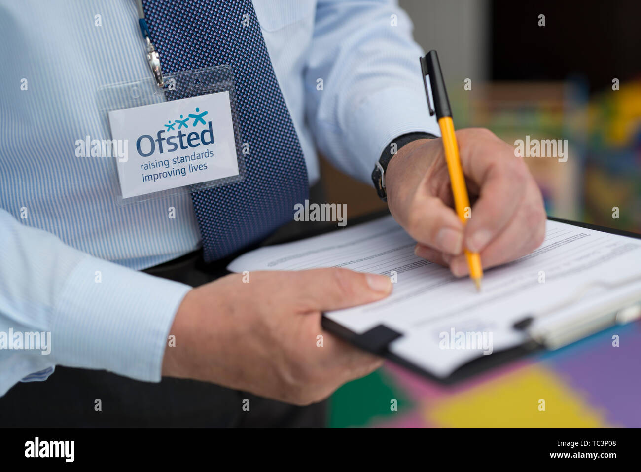 A man dressed in a shirt and tie with an Ofsted lanyard appears to be compiling a report using a pen and clipboard. (Editorial use only) Stock Photo
