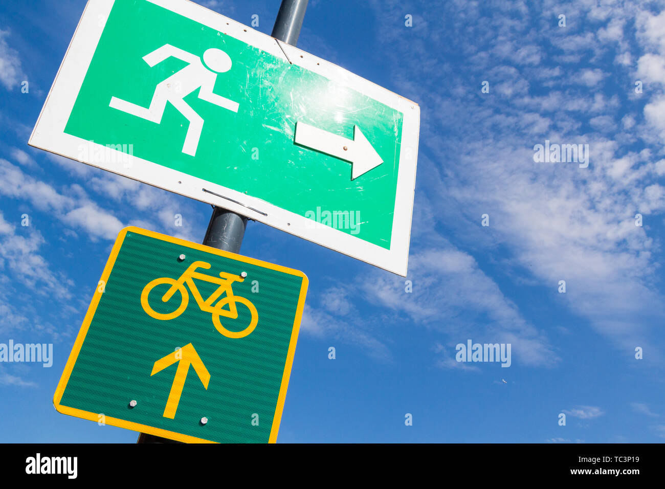 Emergency exit and bike route sign fixed on street lamp pole against blue sky Stock Photo