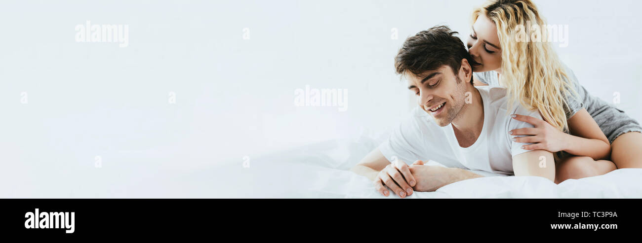panoramic shot of happy blonde girl hugging handsome boyfriend lying on ...