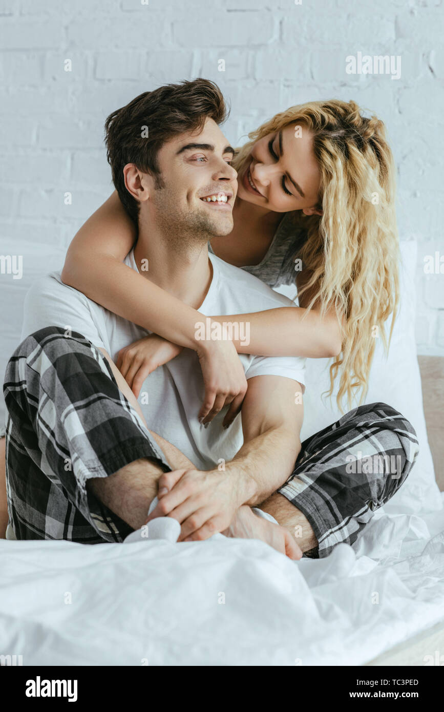 attractive blonde woman hugging happy boyfriend sitting on bed Stock ...