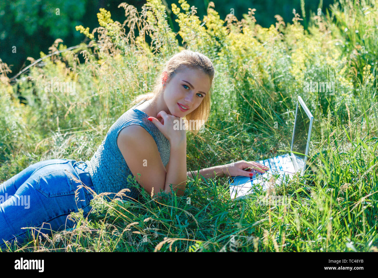 Girl with a laptop in nature lying on the grass. The concept of combining leisure and work. Individual entrepreneur. Stock Photo