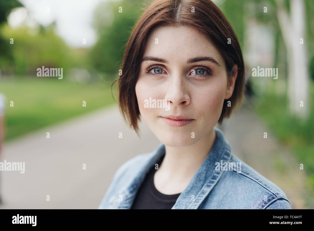 Close up portrait of a thoughtful young woman staring earnestly at the camera with a serious expression outdoors in an urban park Stock Photo