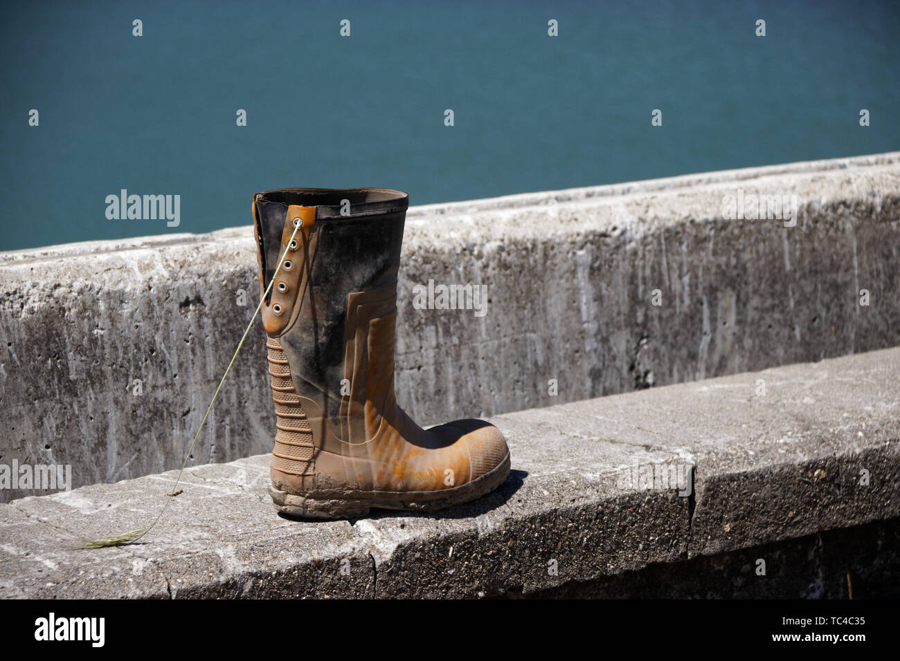 One lace up rubber boot, muddy and discarded at the sea front. Stock Photo