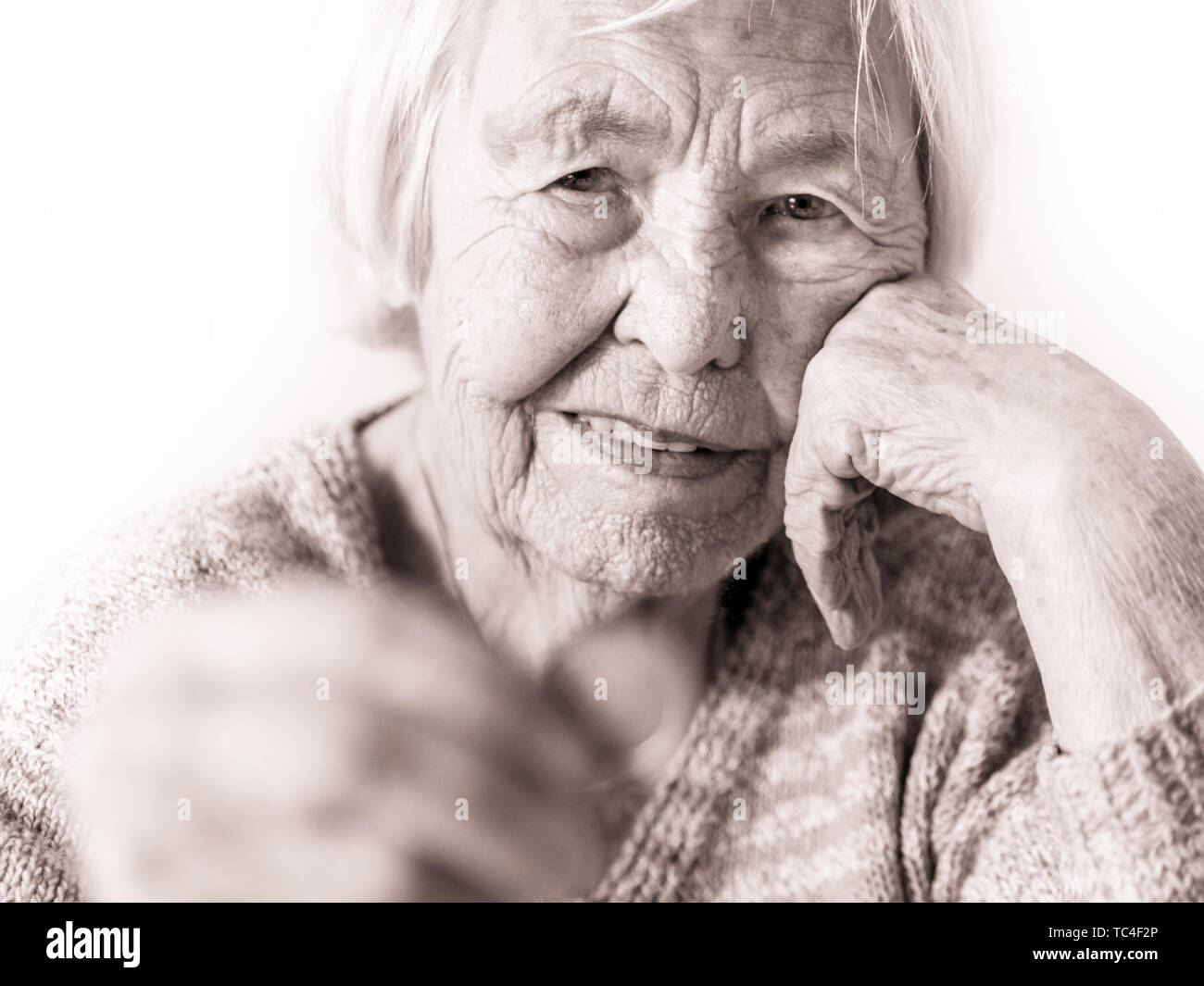 Sad elderly woman sitting at the table at home and looking miserably at only remaining coin from pension in her hand. Stock Photo