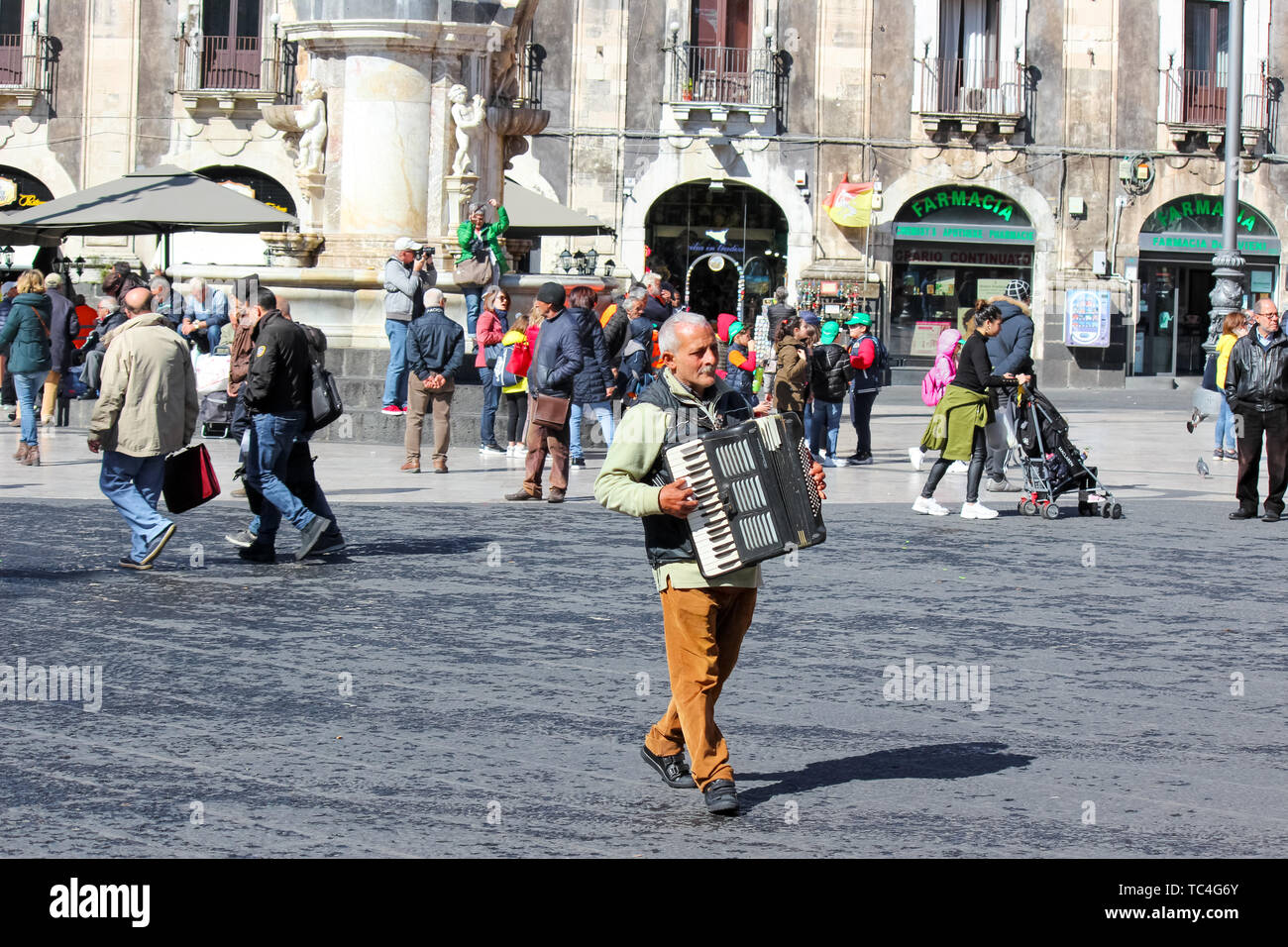 Catania, Sicily, Italy - Apr 10th 2019: Older man busker playing accordion on the Piazza Duomo square in the city center. Cultural street performance. Stock Photo