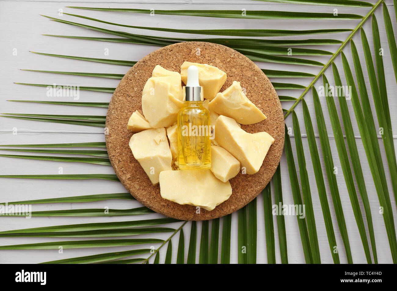 Cocoa butter, bottle of essential oil and palm leaf on table Stock