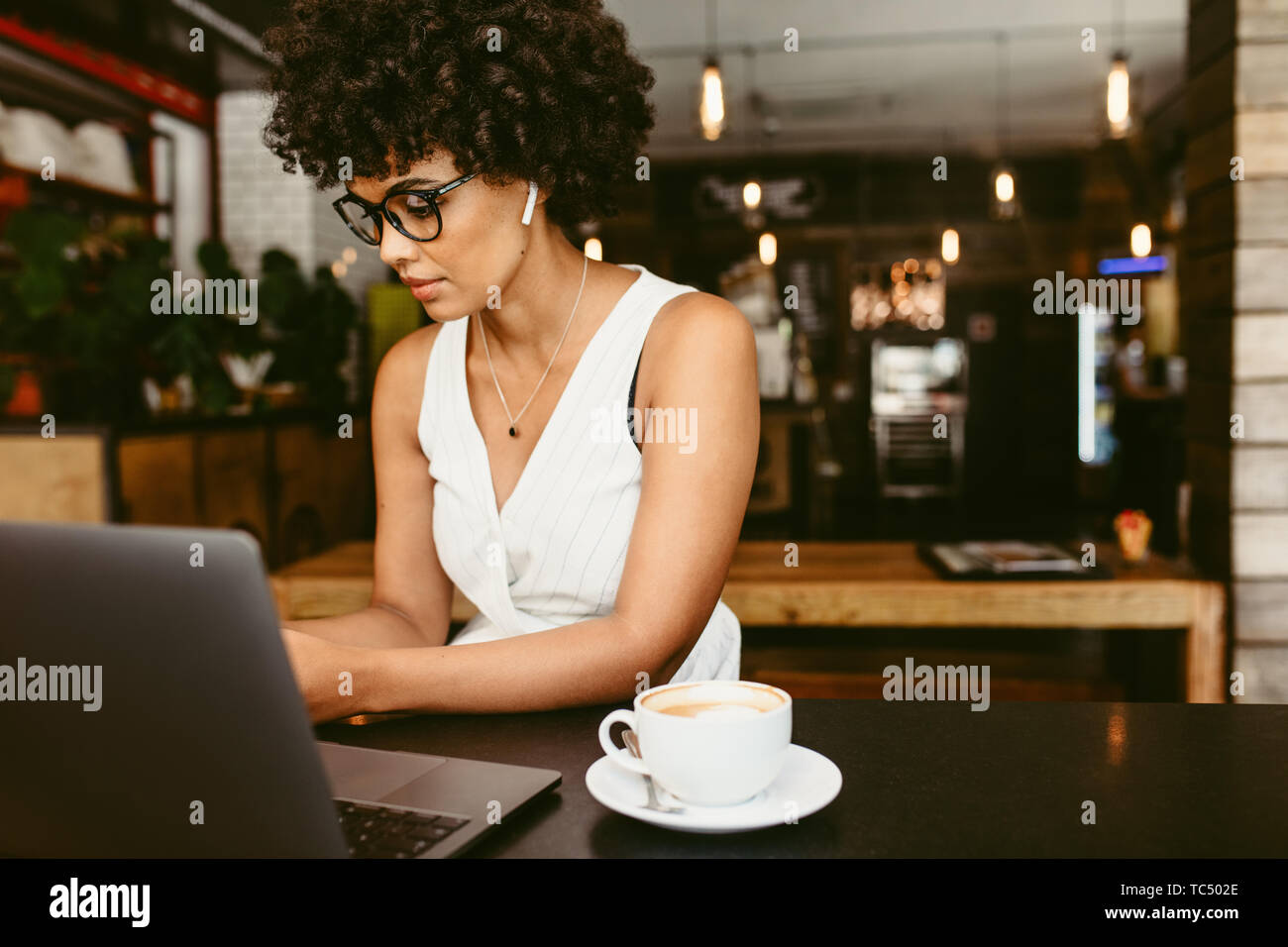 African woman sitting at cafe with laptop and cup of coffee on table. Young woman working at a cafe. Stock Photo