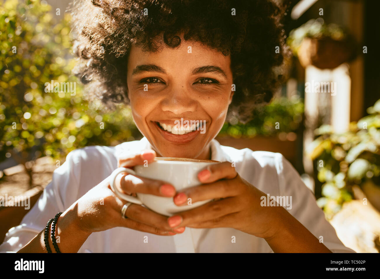 Close up of a woman with a cup of coffee sitting at cafe. African female having a coffee at outdoor coffeeshop. Stock Photo