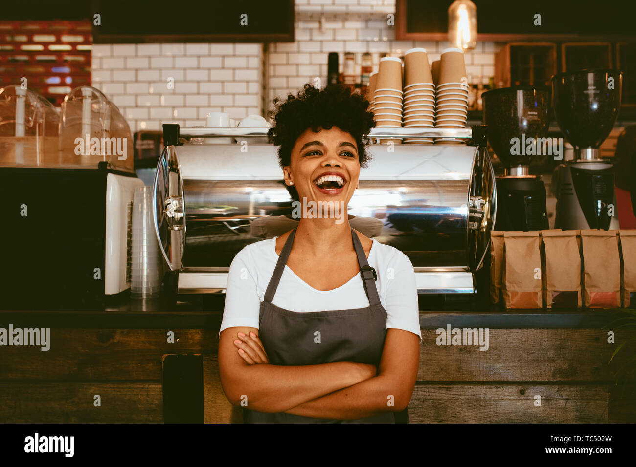 Woman barista inside her coffee shop. Woman bartender in cheerful mood standing in front on the counter. Stock Photo