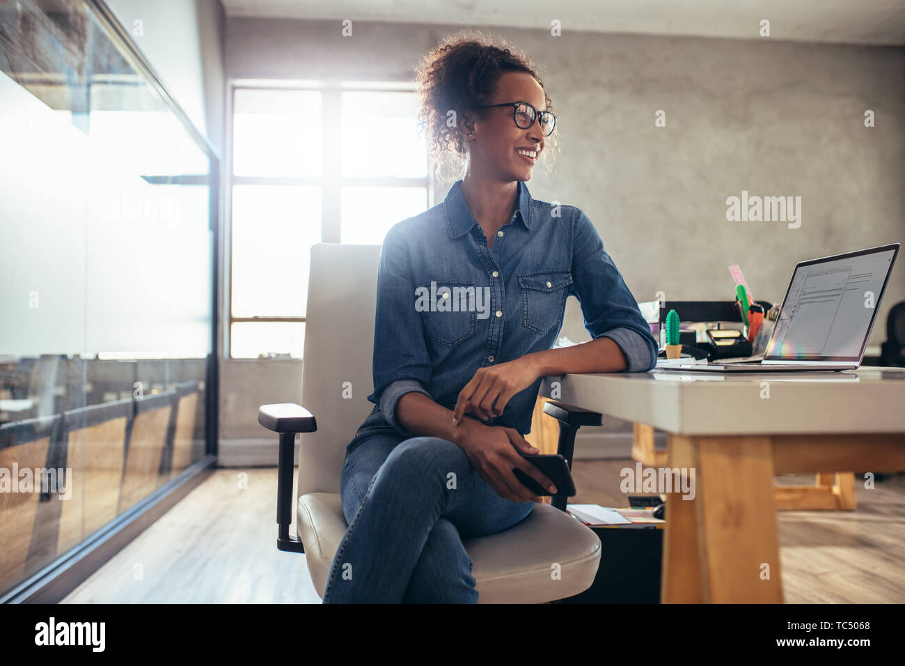Young woman entrepreneur sitting at her desk and looking away. Businesswoman at work in a small office. Stock Photo