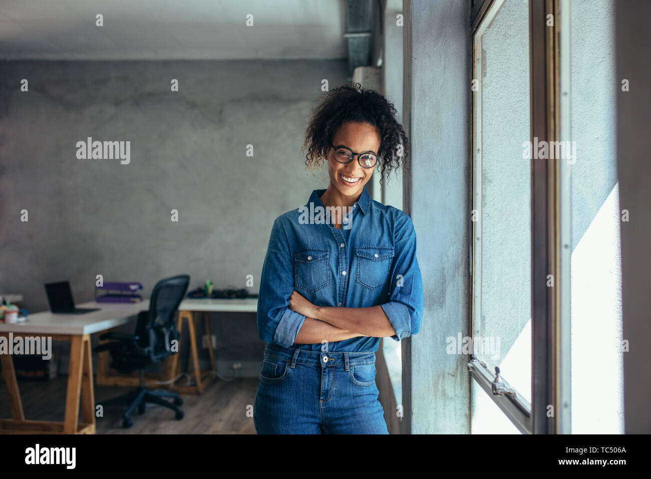 Confident entrepreneur standing in office with her arms crossed. Smiling young businesswoman standing in office and looking at camera. Stock Photo