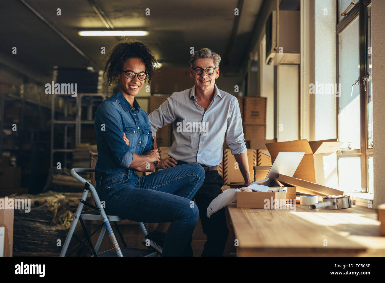 Portrait of man and woman standing in online store warehouse. Business partners together looking at camera and smiling. Stock Photo