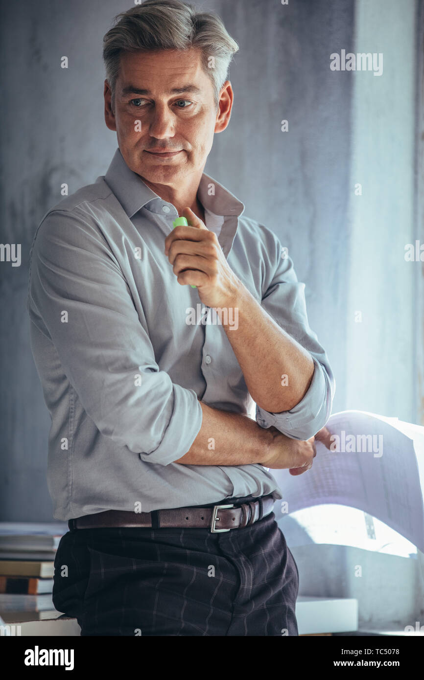 Mid adult male entrepreneur in office looking away and thinking. Mature man at his office looking pensive. Stock Photo