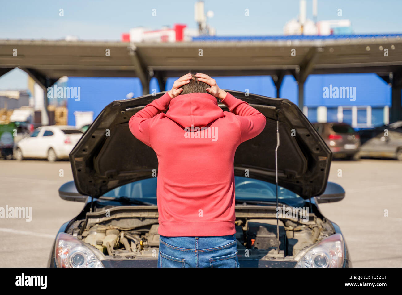Photo on back of man next to open hood of broken car in daytime Stock