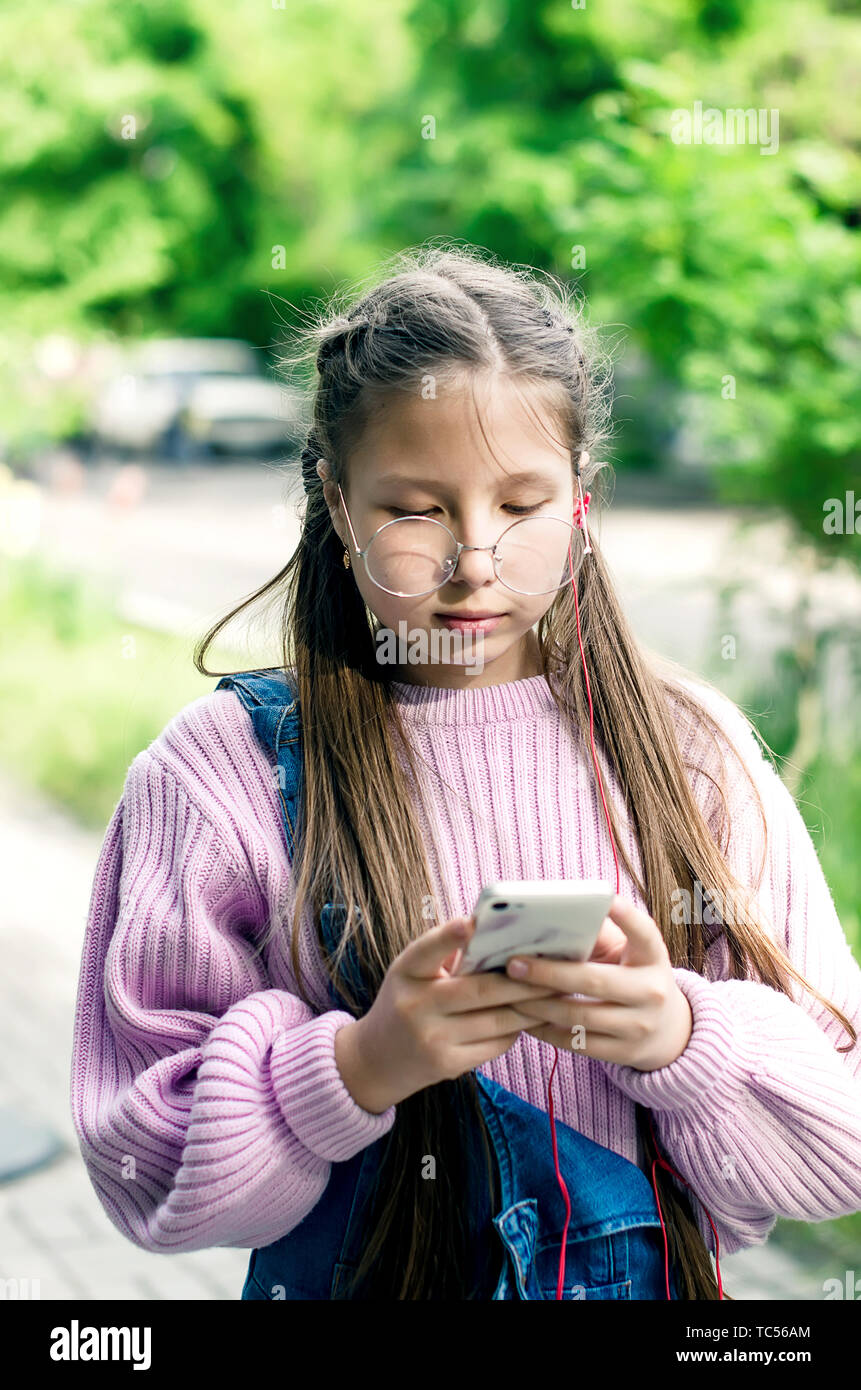 girl teenager in round glasses and denim overalls and a pink sweater looks  into the phone Stock Photo - Alamy
