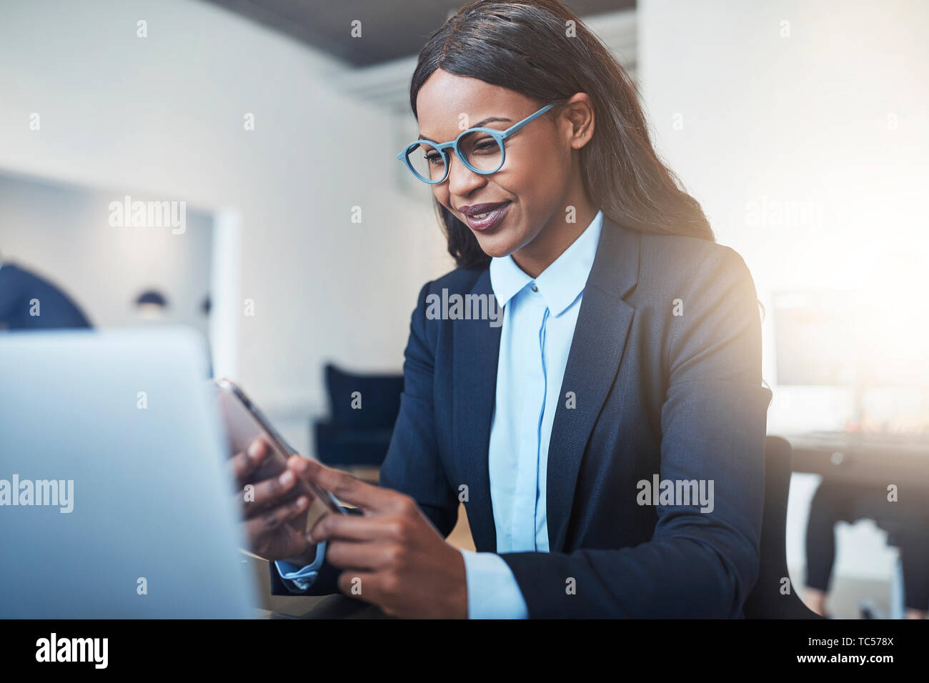 Smiling young African American businesswoman sending a text message and ...